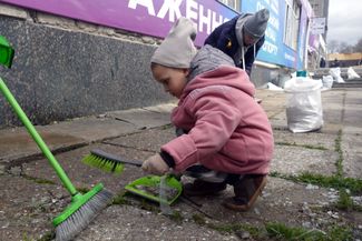 Ребенок собирает в совок осколки стекла, выбитого в результате российского обстрела