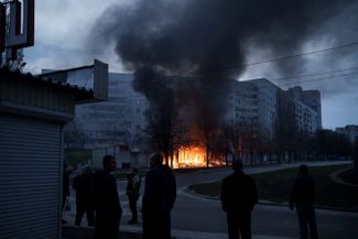 Жители харьковской многоэтажки наблюдают, как магазины возле их дома горят после обстрела.