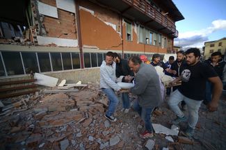 Спасатели и местные жители несут пострадавшего при землетрясении