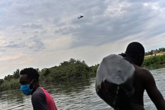 Вертолет над головами мигрантов, переходящих Рио-Гранде, 21 сентября 2021 года