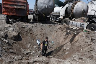 Местный житель на фоне грузовиков, разрушенных в результате российского обстрела. 