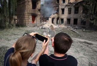 Местные жители фотографируют горящее здание химического техникума, которое российские войска обстреляли утром 26 августа<br>