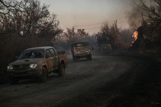 Military vehicles of the Armed Forces of Ukraine drive past a fire that occurred after explosions of phosphorus ammunition