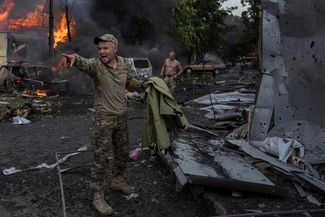 Украинский военнослужащий зовет парамедиков. За ним лежат тела погибших 