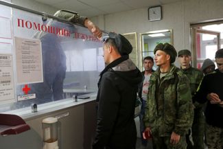 Дежурный измеряет температуру мобилизованных жителей Волгограда, стоящих в очереди на регистрацию в военкомате