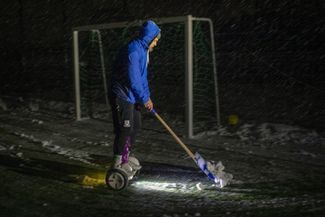 Украинец на ховерборде очищает от снега футбольное поле в Ирпене. Там собираются играть почти в полной темноте. 29 ноября 2022 года