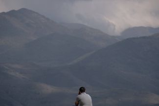 A man talking on a phone gazes at the mountains of Nagorno-Karabakh in the distance. Kornidzor, Armenia.