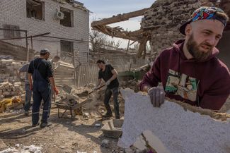 Местные жители убирают обломки разрушенного дома после российского ракетного обстрела