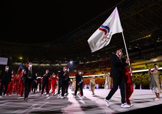 Максим Михайлов с флагом ОКР (белое полотнище с пятью олимпийскими кольцами и тремя языками пламени в цветах флага РФ), под которым выступают атлеты из России