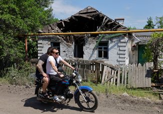 Жители Макеевки проезжают мимо частного дома, разрушенного недавним обстрелом