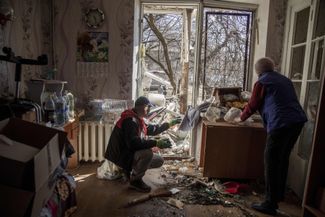 Жители разрушенного ракетным ударом дома прибираются в своей квартире