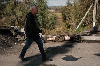 Прохожий идет мимо убитого российского военного, пока украинцы эвакуируются из освобожденного Купянска