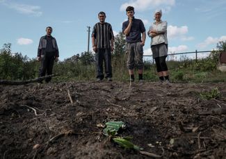 Жители села Каменка Харьковской области стоят возле противопехотной мины у своего дома. Сентябрь 2022 года