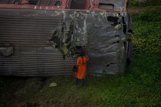 Женщина заглядывает в разрушенный вагон, лежащий рядом с железнодорожными путями. 4 июня 2023 года