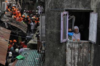Жительница индийского города Мумбаи на фоне спасателей, которые ищут людей в рухнувшем здании. 16 июля 2019 года