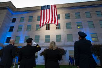 Председатель Объединенного комитета начальников штабов генерал Марк Милли (второй слева) отдает честь американскому флагу на стене Пентагона на рассвете в день 20-летия терактов 11 сентября. 