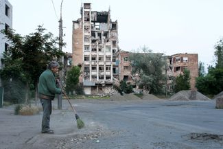 A resident of Russian-occupied Mariupol sweeps the street in front of a bombed-out residential building. June 11, 2023.
