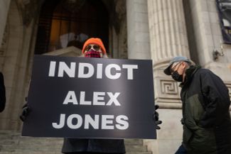Активист в первую годовщину штурма Капитолия держит плакат с требованием осудить Алекса Джонса. Нью-Йорк, 6 января 2022 года