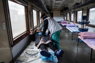 Сотрудник «Врачей без границ» помогает пострадавшей женщине в медицинском поезде перед эвакуацией с линии фронта