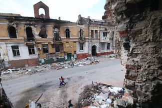 Дети идут среди разрушенных зданий в Мариуполе