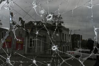 Отражение здания в Днепре, поврежденного российским ракетным ударом, в разбитом окне