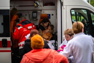 Работники госпиталя переносят детей и медицинское оборудование в машину скорой помощи