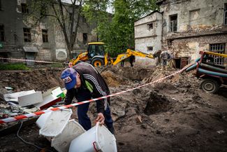 Работник больницы выносит вещи из уцелевшего здания на фоне воронки от попадания российской ракеты. 